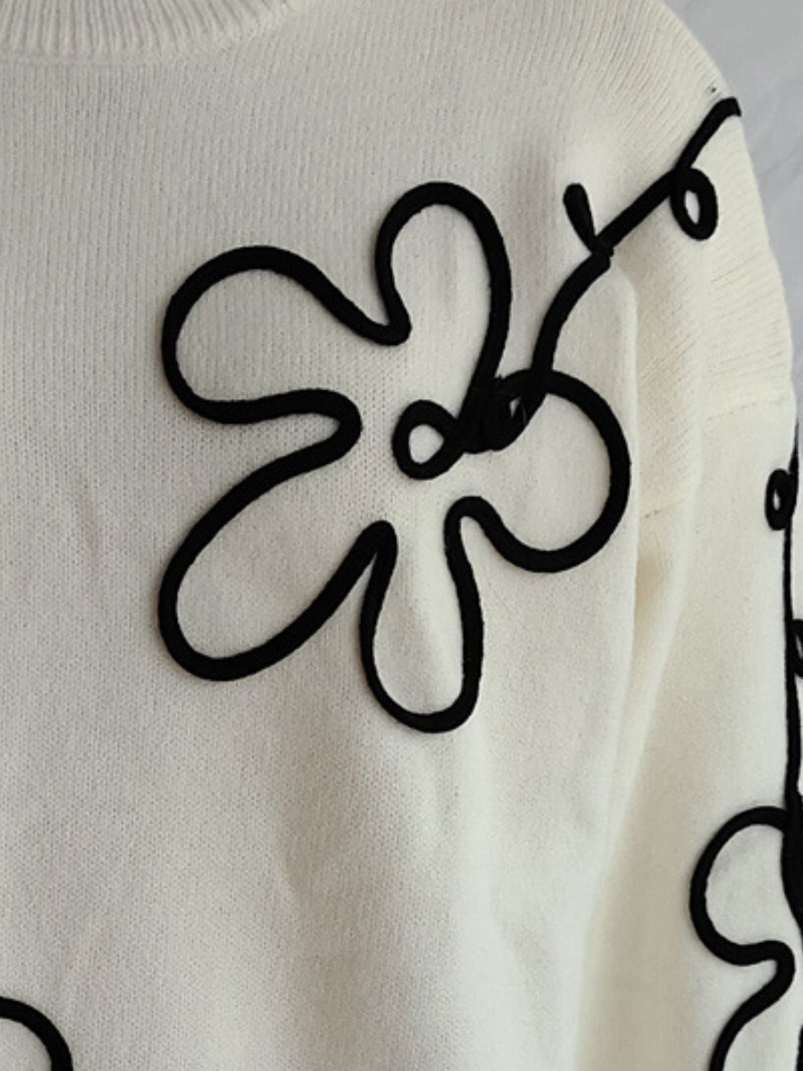 Beige knit sweater with black floral outline embroidery, crew neck, long sleeves.
