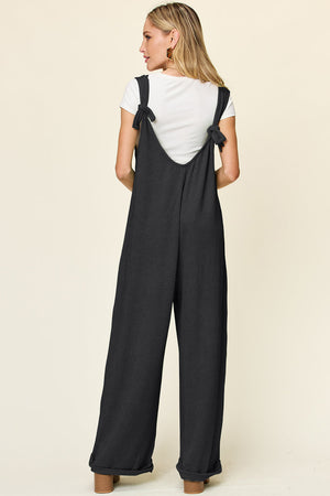 Black ribbed knit tie-strap jumpsuit with wide legs, worn with a white tee.