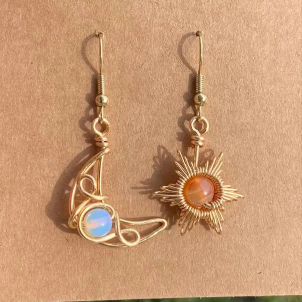 Gold celestial asymmetrical drop earrings with moon and sun charms and gemstone accents.