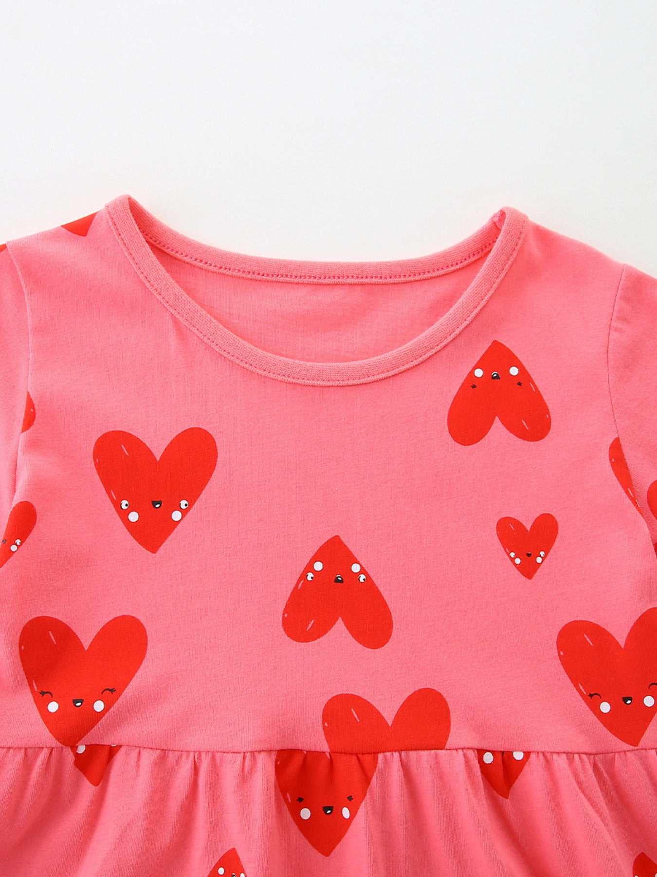 Pink cotton baby dress with red heart print and ruffled hem.