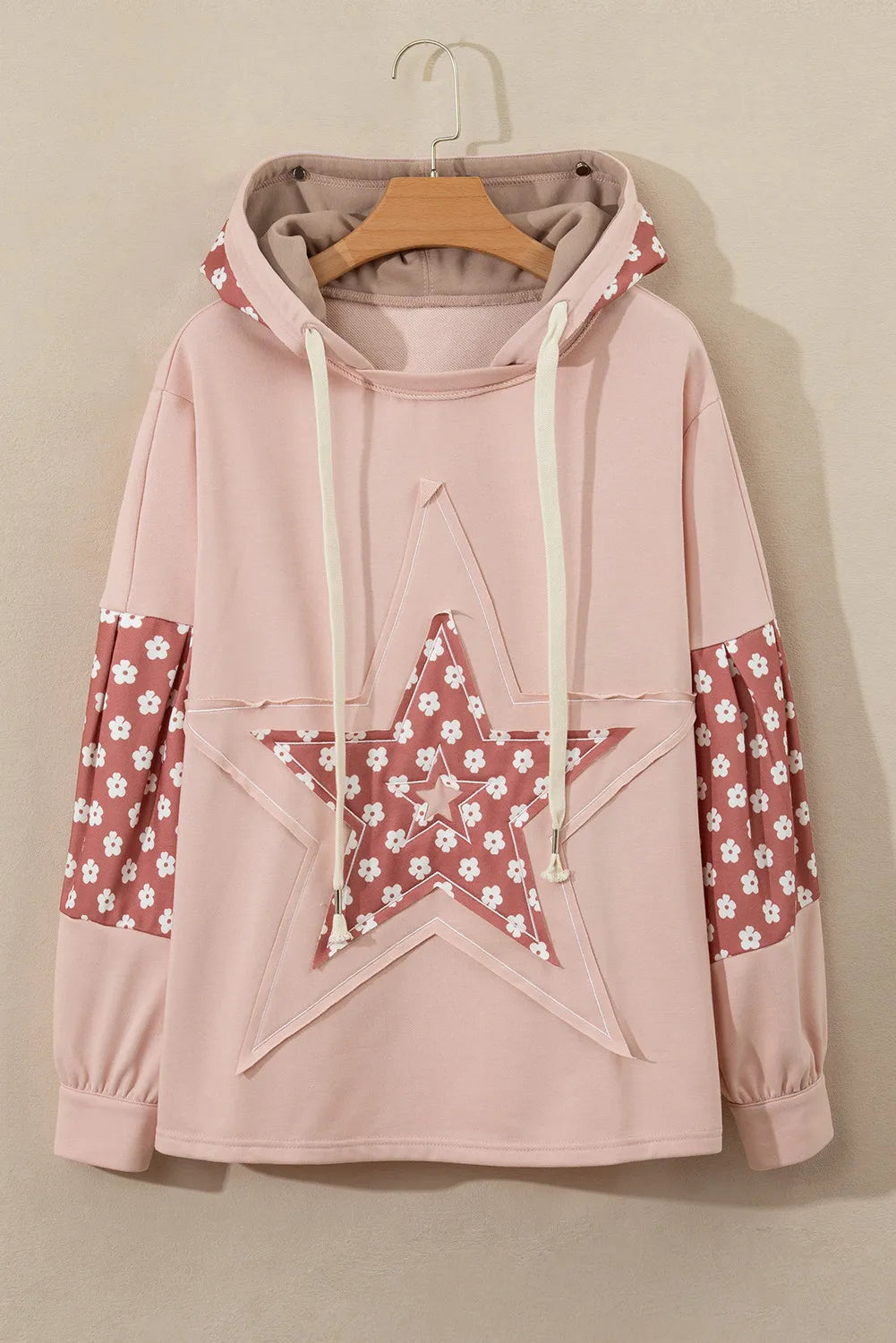 Dusty pink hoodie with floral star patchwork on front and sleeves, drawstring hood.
