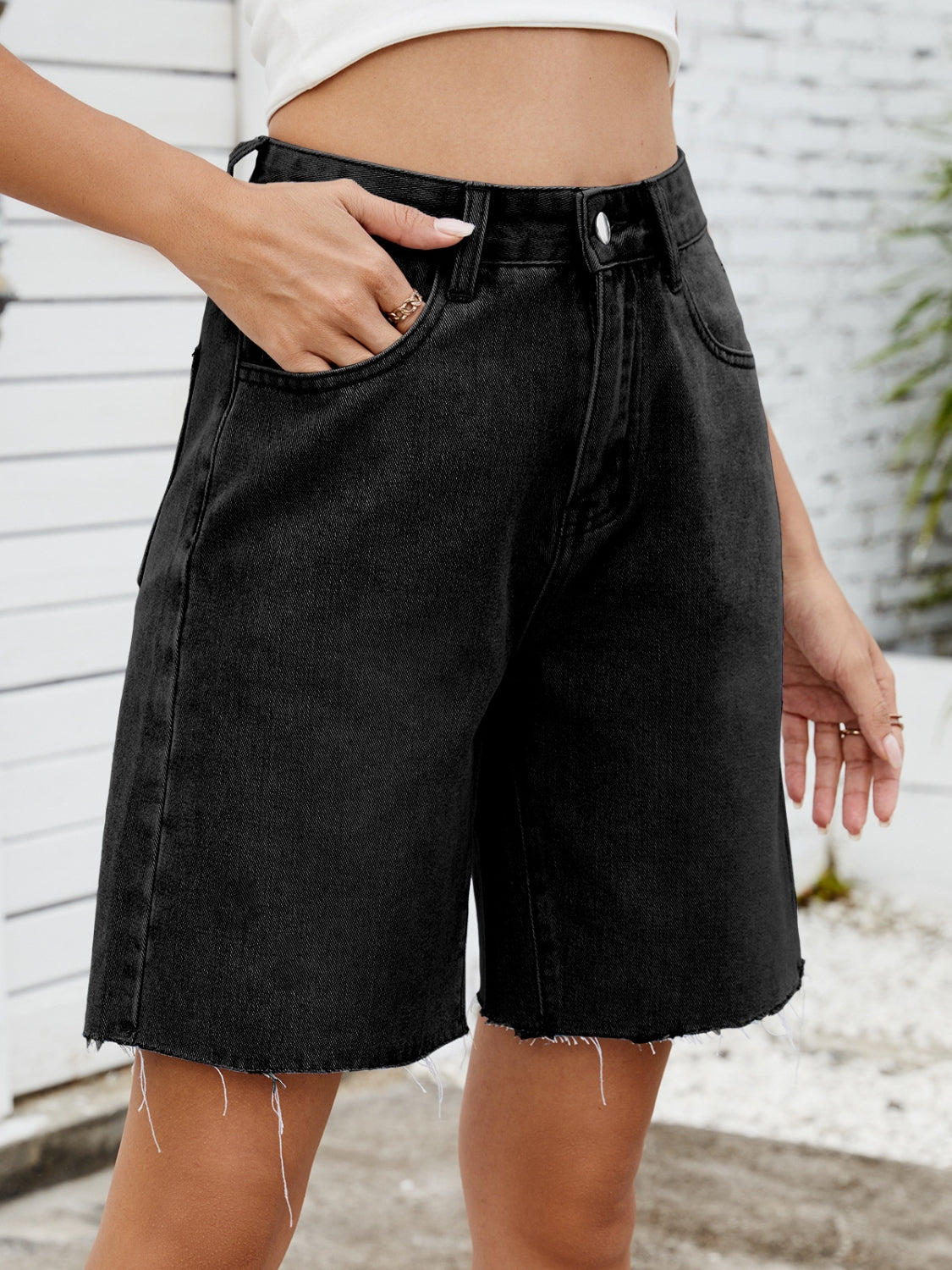 Black longline denim cutoff shorts with raw hem detail.
