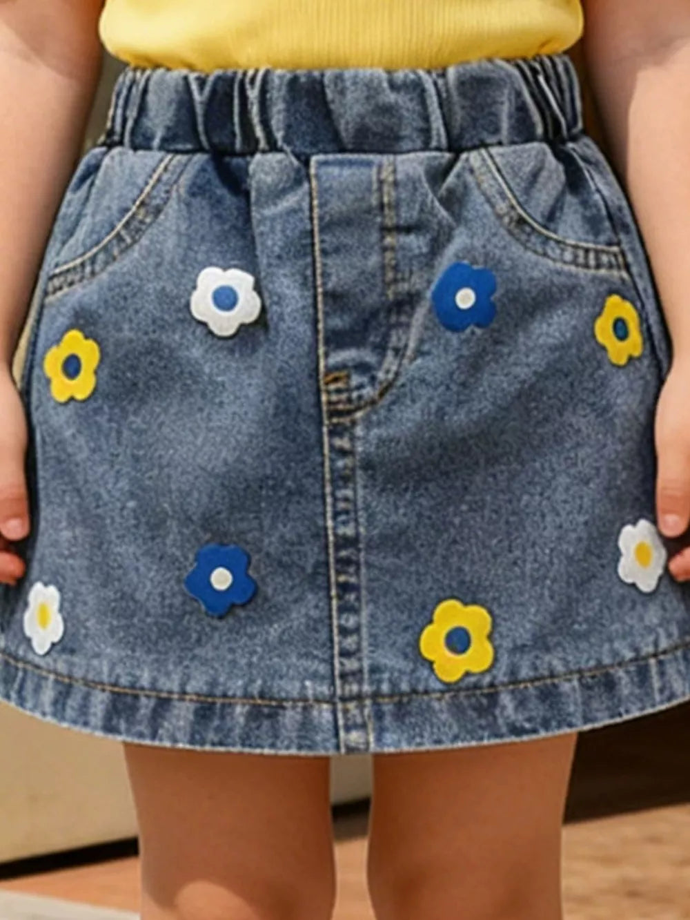 Denim A-line skirt with elastic waist and colorful flower appliqus.