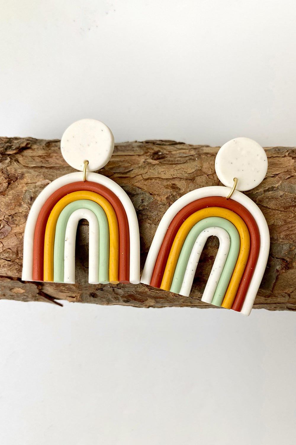 Rainbow arch clay earrings in white, rust, yellow, green, and ivory.