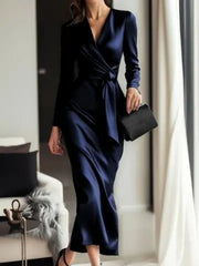 Luxurious satin tie-waist dress in dark blue with V-neck and long sleeves.