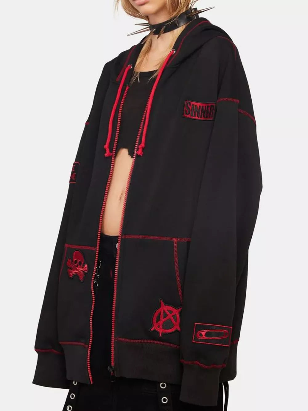 Black zip-up hoodie with red contrast stitching and graphic patches like skull and anarchy symbol.