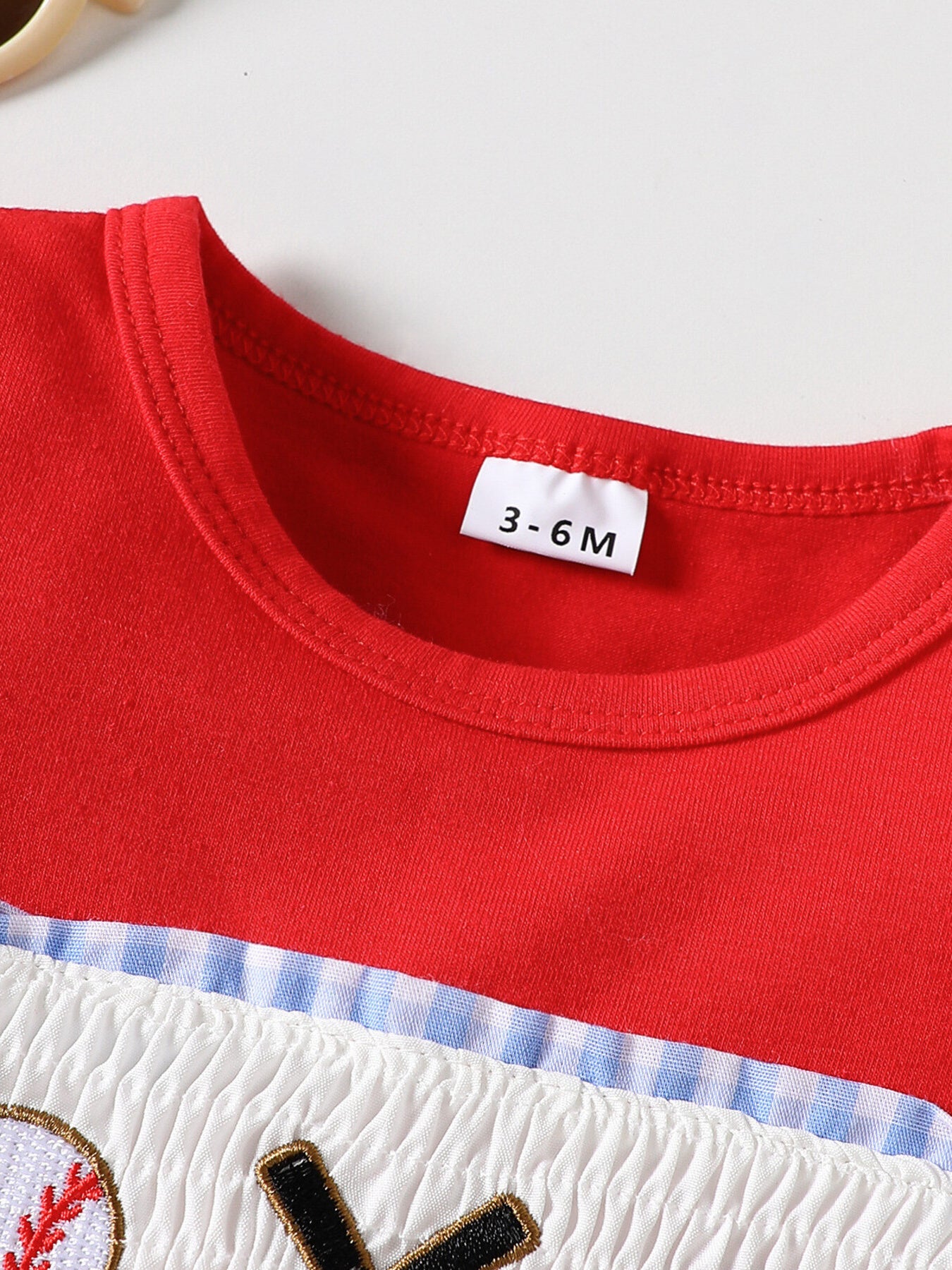 Red baseball graphic tee with smocked white fabric and blue gingham trim.