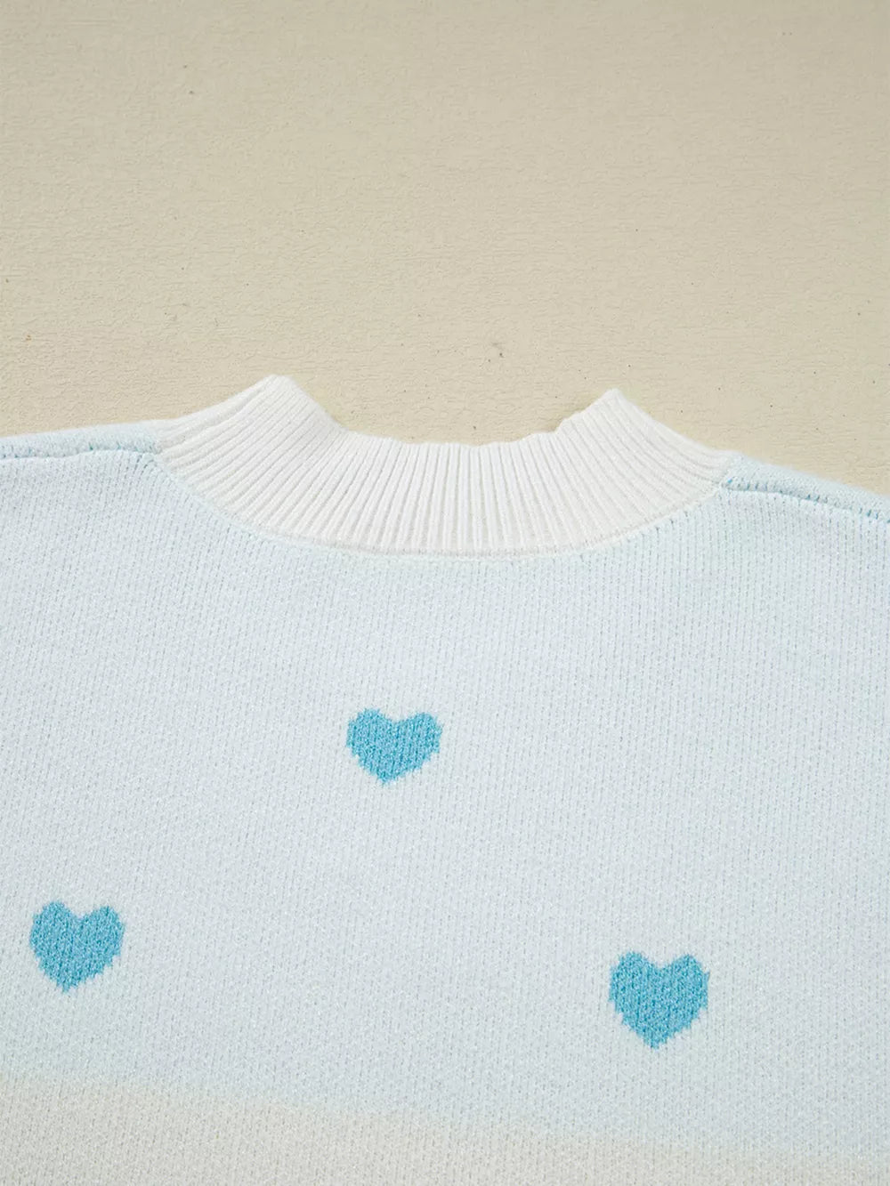 Light blue knit sweater with white crew neck and scattered blue hearts pattern.