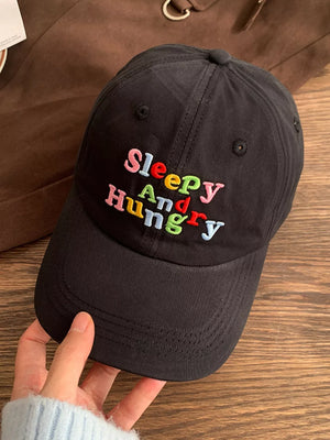 Black cotton baseball cap with colorful embroidered "Sleepy And Hungry" text.