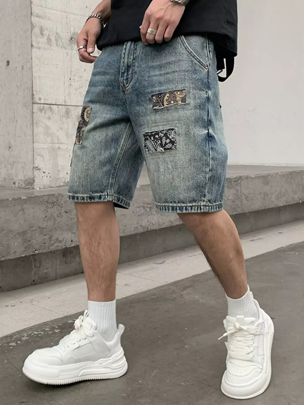 Men's denim shorts in light wash blue with graphic patchwork details and a relaxed fit.