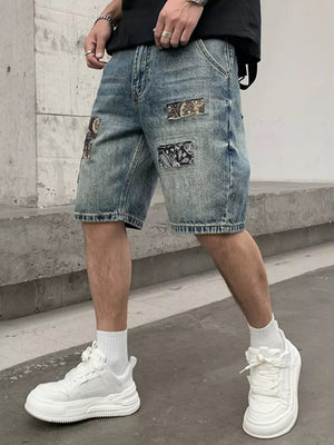 Men's denim shorts in light wash blue with graphic patchwork details and a relaxed fit.