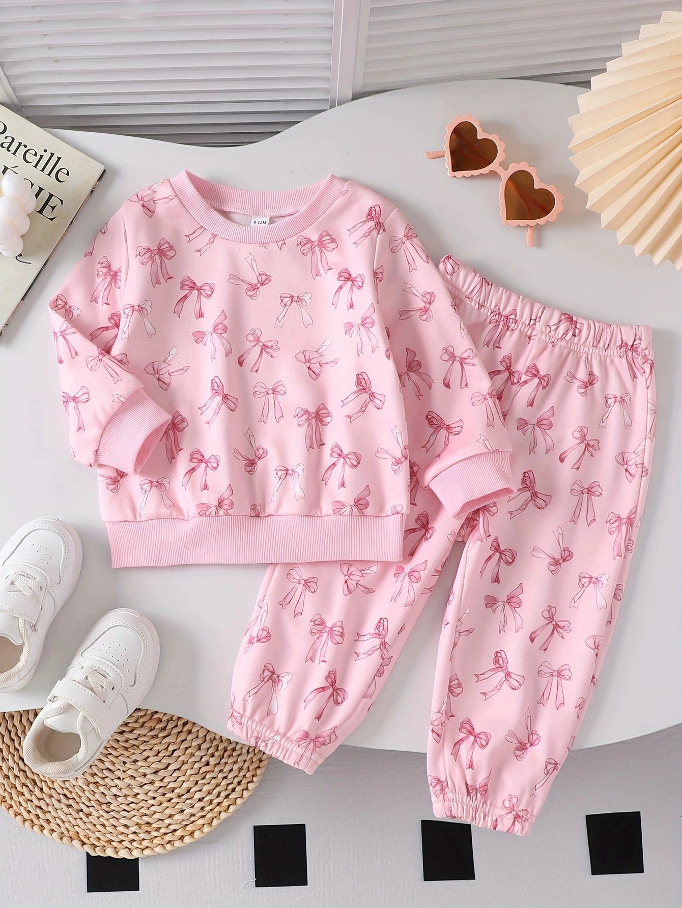 Pink baby tee and pants set with a bow print, crew neck, long sleeves, and elastic waistband.
