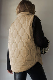 Beige quilted stand-collar utility gilet with a wave pattern, worn over a black sweater.