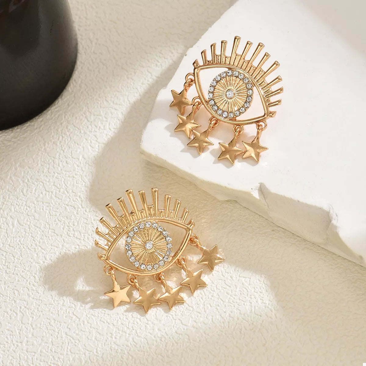 Gold evil eye dangle earrings with stars and rhinestones.