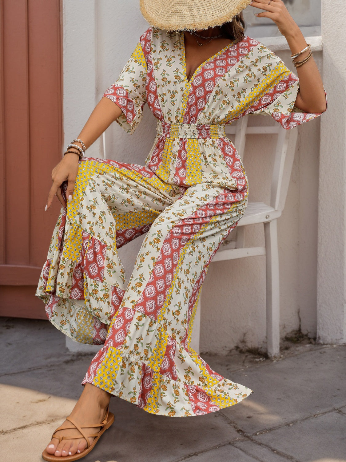 Bohemian print palazzo jumpsuit with V-neck, flutter sleeves, and ruffled wide legs in multicolor.