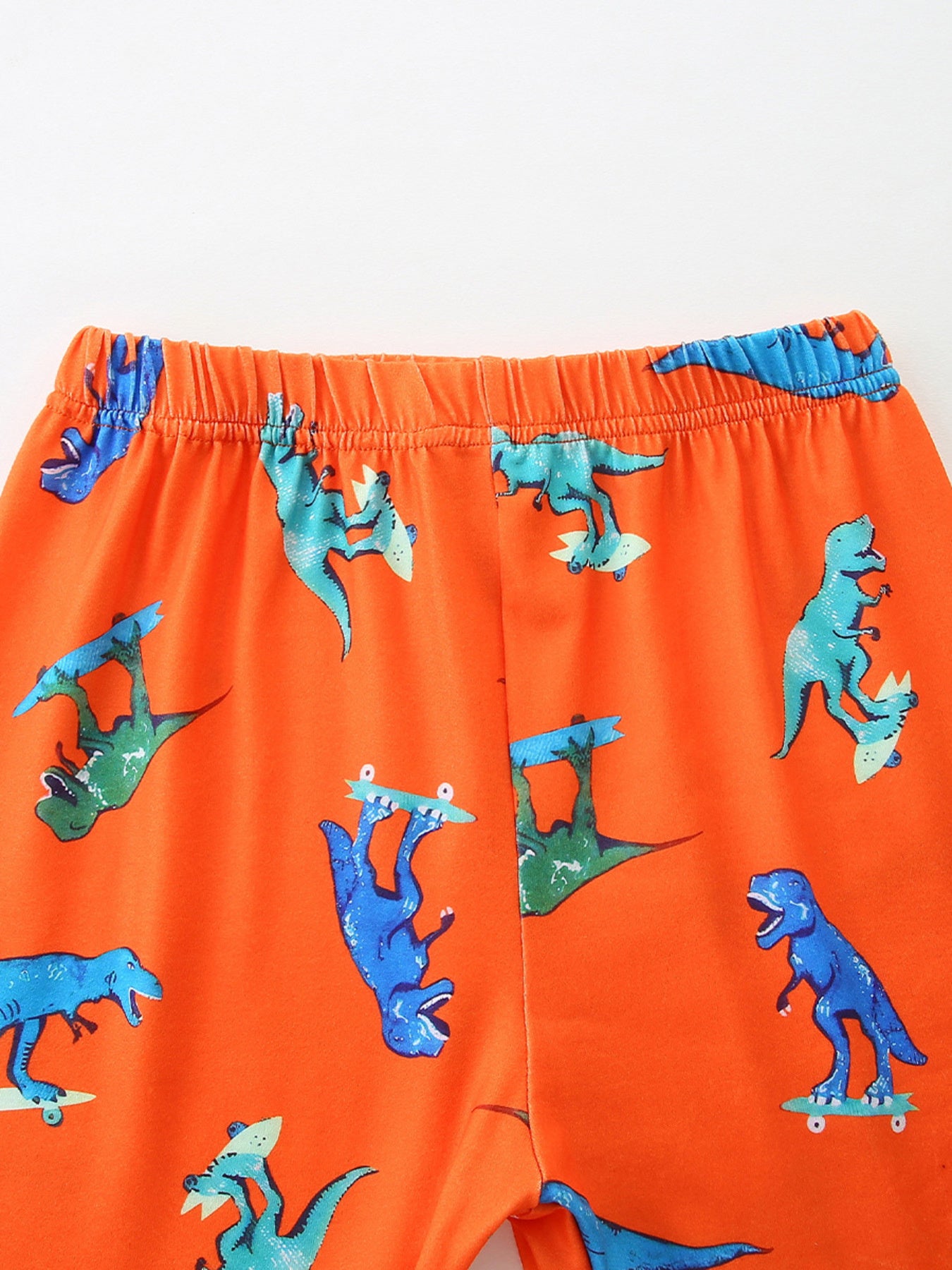 Orange toddler shorts with skateboarding dinosaurs pattern