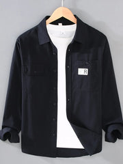Black cotton long-sleeve overshirt with two chest pockets and button closure, worn over a white t-shirt.