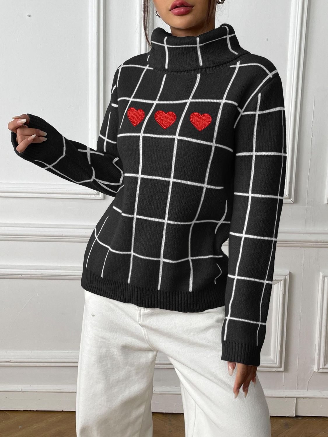 Black turtleneck sweater with white grid pattern and three red heart appliqués.