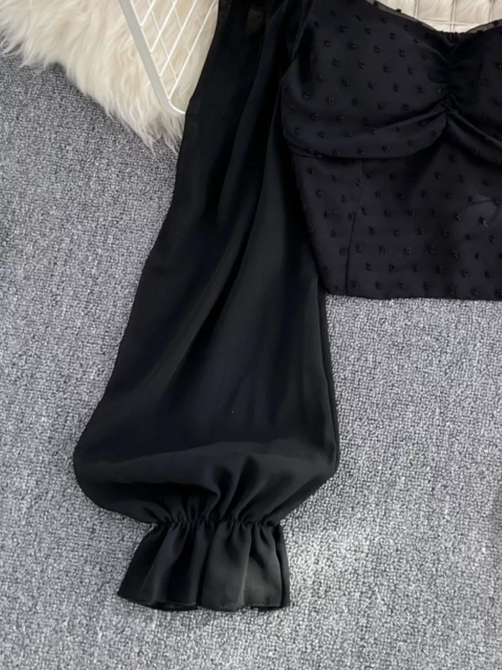 Black Swiss dot maternity blouse with ruffled sleeve cuff and ruched bodice detail.