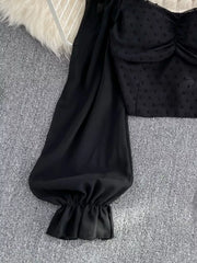 Black Swiss dot maternity blouse with ruffled sleeve cuff and ruched bodice detail.