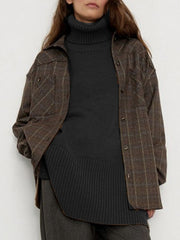 Black ribbed turtleneck sweater with flared sleeves, layered under a plaid shirt jacket.
