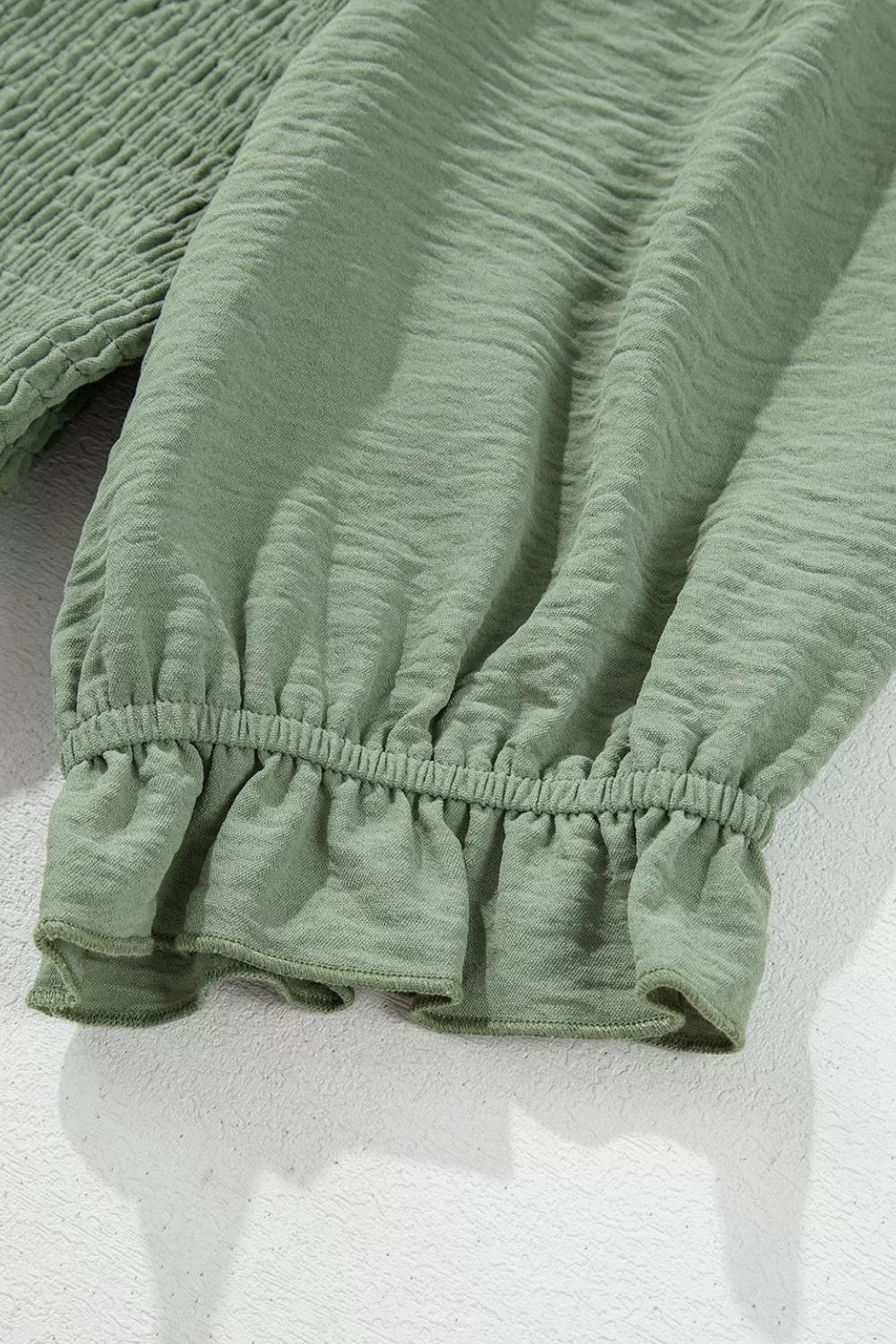 Sage smocked mini dress with ruffled hem and textured fabric.