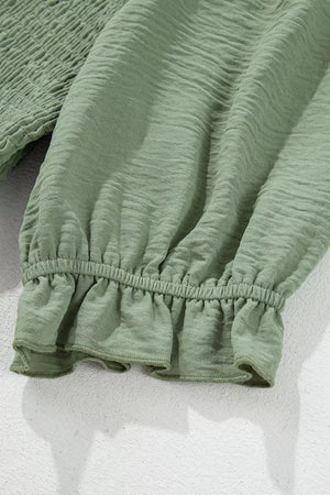 Sage smocked mini dress with ruffled hem and textured fabric.