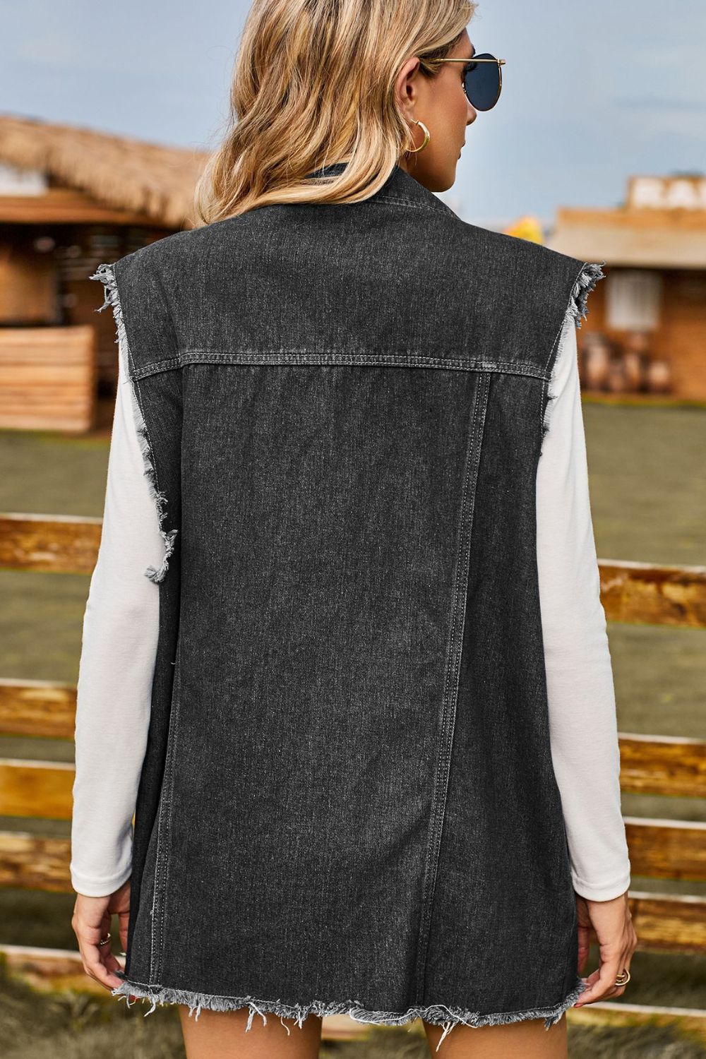 Dark distressed denim sleeveless jacket with frayed hem and armholes.