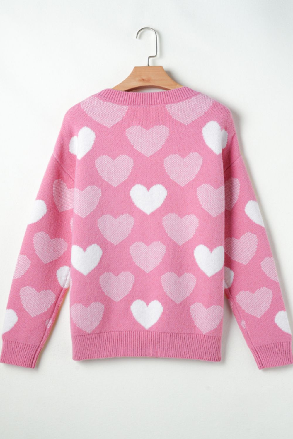 Pink intarsia knit sweater with allover white heart pattern and pearl embellishments.