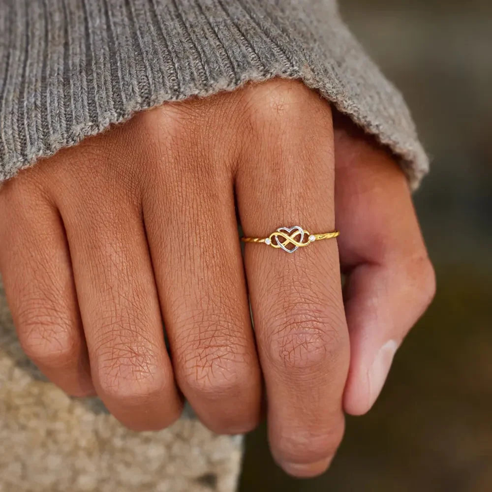 Gold intertwined heart and infinity ring on a finger.