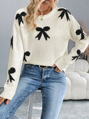 Cream knit crewneck sweater with scattered black bow pattern, long sleeves, and crew neckline.