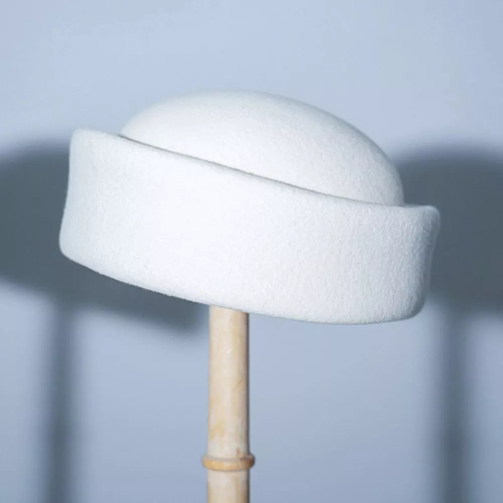 White wool pillbox hat with a curved brim, displayed on a stand.
