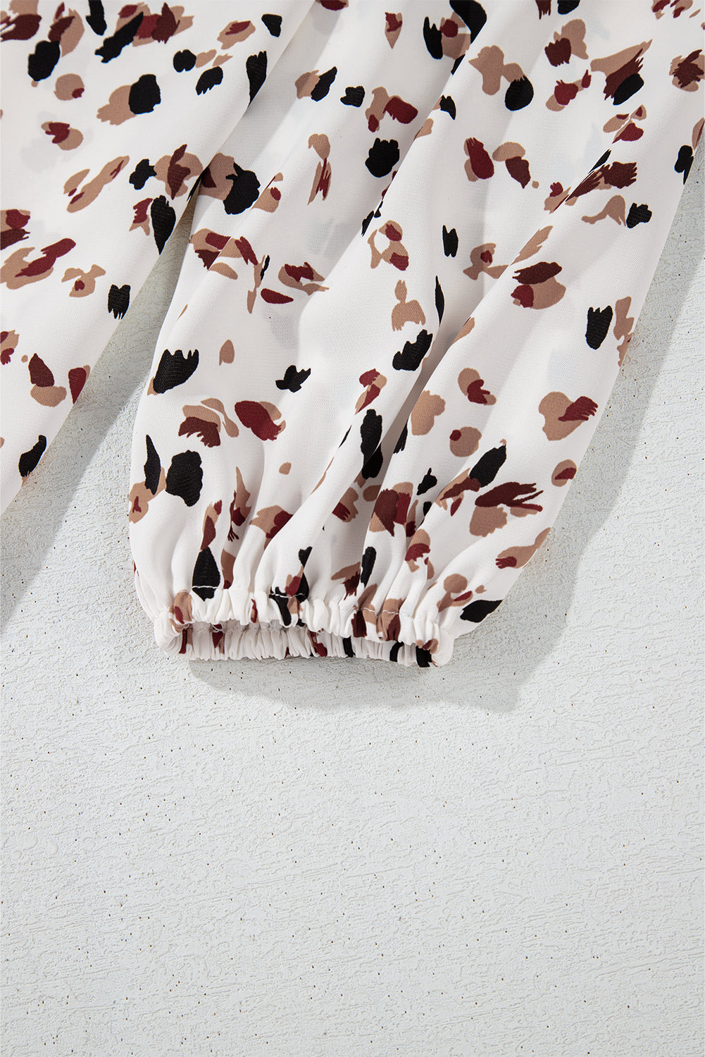 High-neck abstract print blouse in white with black and brown spots, featuring a gathered elastic cuff.