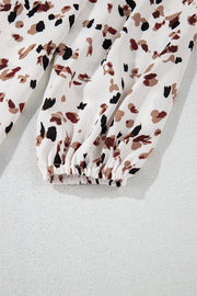 High-neck abstract print blouse in white with black and brown spots, featuring a gathered elastic cuff.