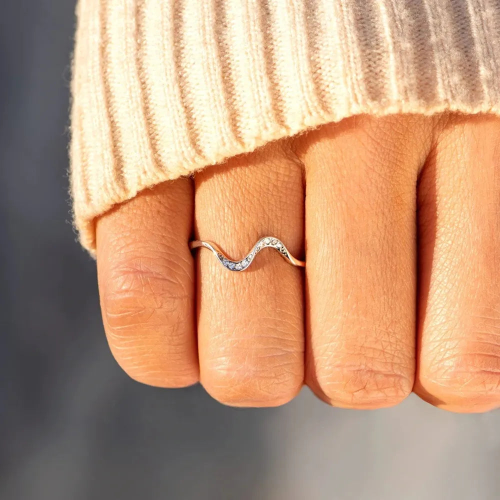 Rose gold serpentine contour ring with pave diamonds on a finger.