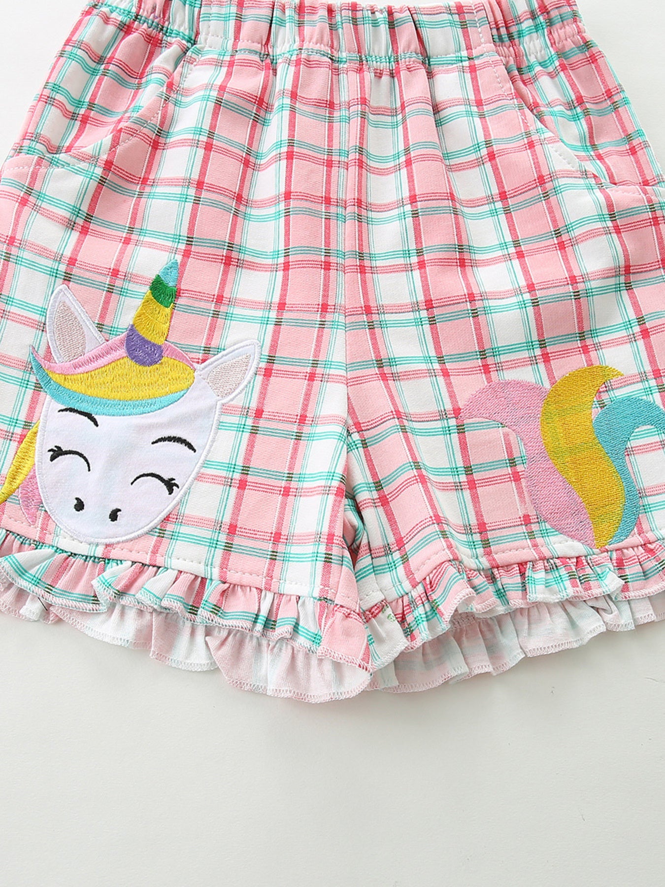 Toddler pink plaid cotton shorts with ruffled hem and unicorn applique.