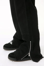 Black bootcut denim pants with zip hem detail and frayed cuffs.