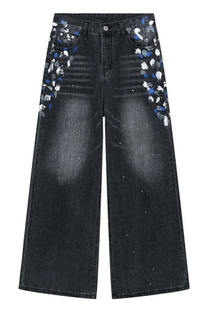 Dark wash denim jeans with painterly blue, white, and grey splatters and a wide flare leg.