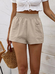 Beige elastic waist shorts with pockets and a relaxed fit, styled with a white crop top.