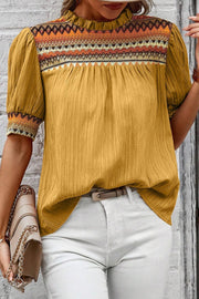 Mustard blouse with embroidered yoke and puff sleeves, featuring a ruffled neckline and textured fabric.