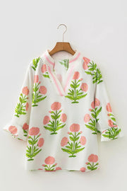 White cotton blouse with pink floral print, notched neckline, and ruffled sleeves.