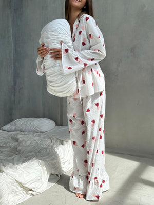 White cotton pajama set with multicolor heart print, collared button-down top and ruffled pants.