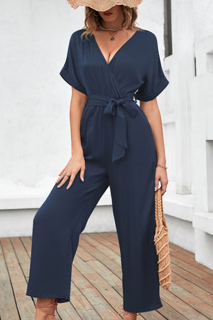 Navy crossover neckline fluid wide leg jumpsuit with belted waist and short sleeves.