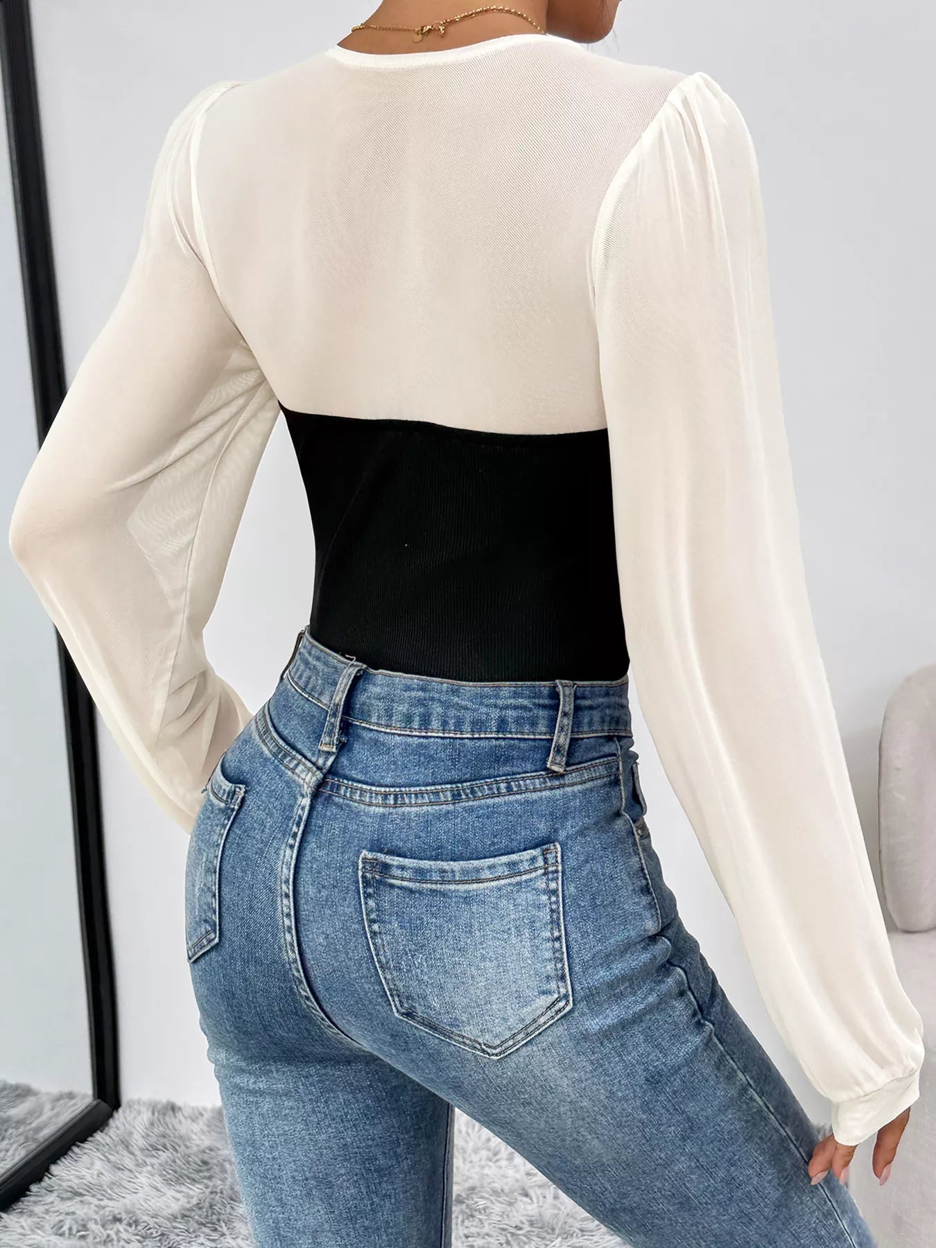 Black and white long-sleeve mesh bodysuit with ribbed black panel, styled with jeans.