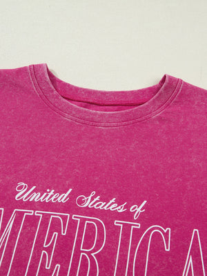 Patriotic graphic cotton t-shirt in faded pink with white "United States of America" text.
