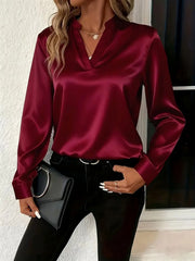 Burgundy satin blouse with notched neckline and long sleeves, styled with black pants and a clutch.