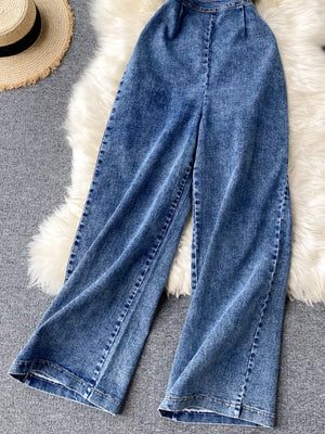 Blue denim wide-leg jumpsuit with halter neck and buttoned front detail.