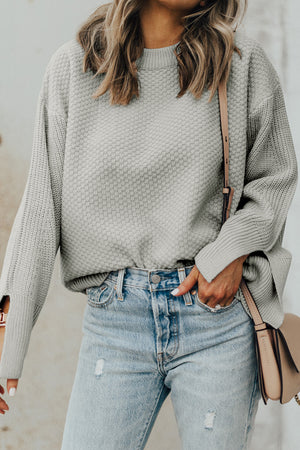 Gray textured knit sweater with crewneck and slit sleeves, styled with jeans.