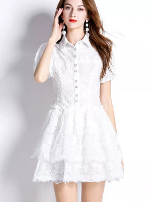 White lace mini dress with puff sleeves, buttoned front, and tiered ruffled skirt.