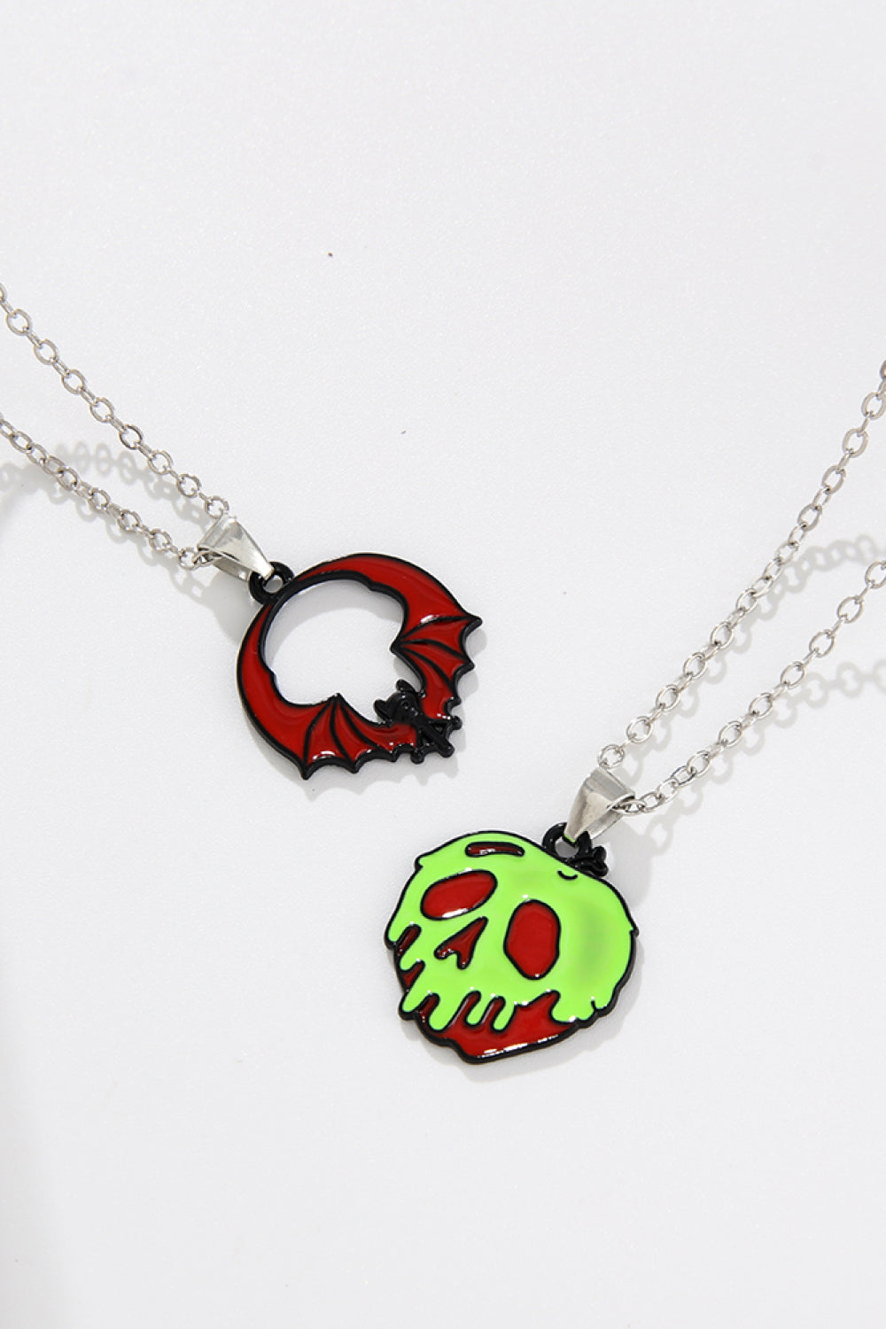 Spooky Season enamel pendant necklaces, one red bat, one green skull with red accents.
